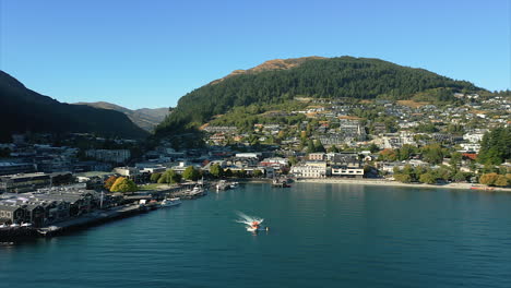 Boat-leaving-port-in-Queenstown,-New-Zealand,-aerial-view-reverse-dolly