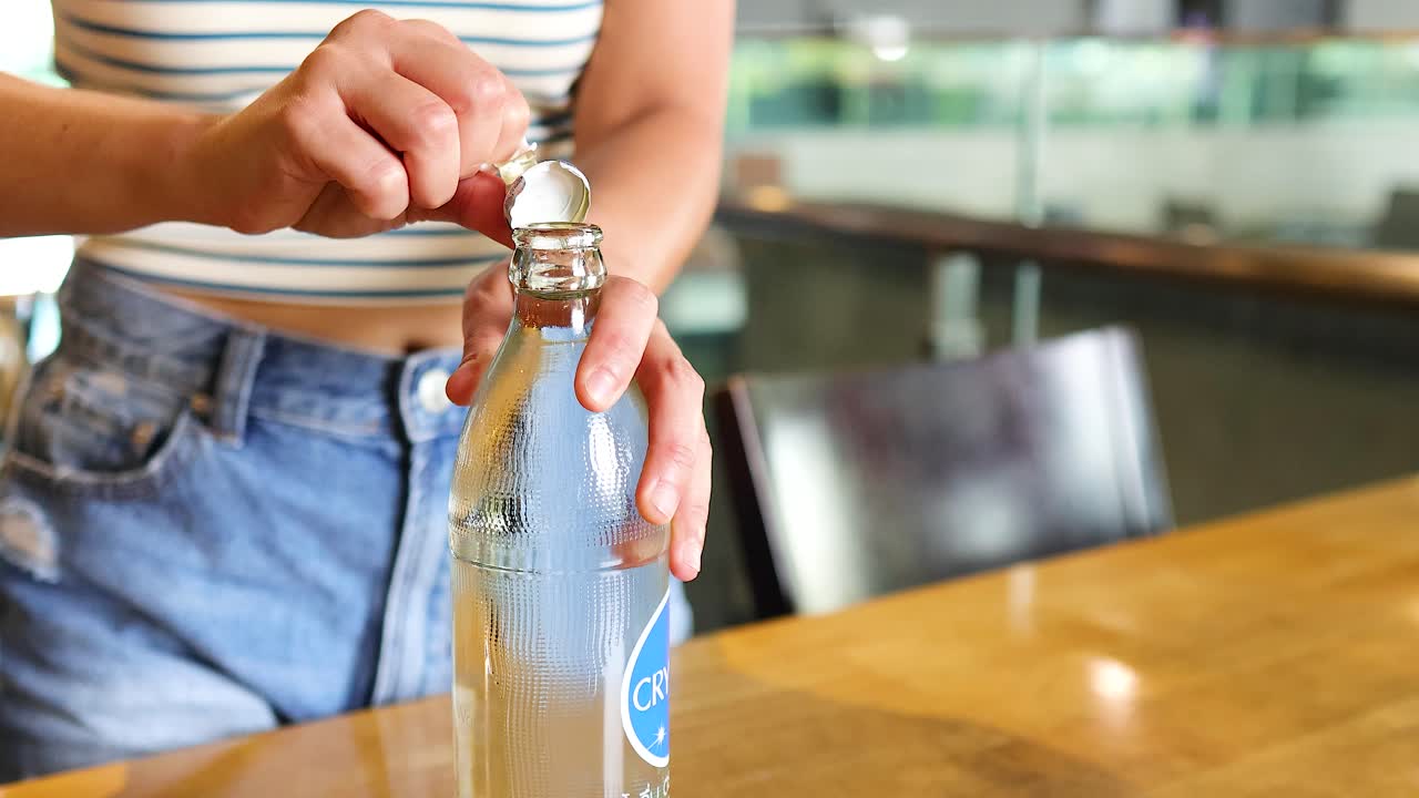A person opens a water bottle on a wooden table in a well-lit Bangkok restaurant, showcasing casual attire and relaxed ambiance