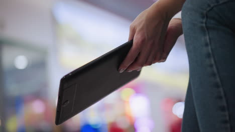 close-up of woman holding tablet in hand with bokeh lighting in background, creating a relaxed and tech-savvy atmosphere in shopping environment