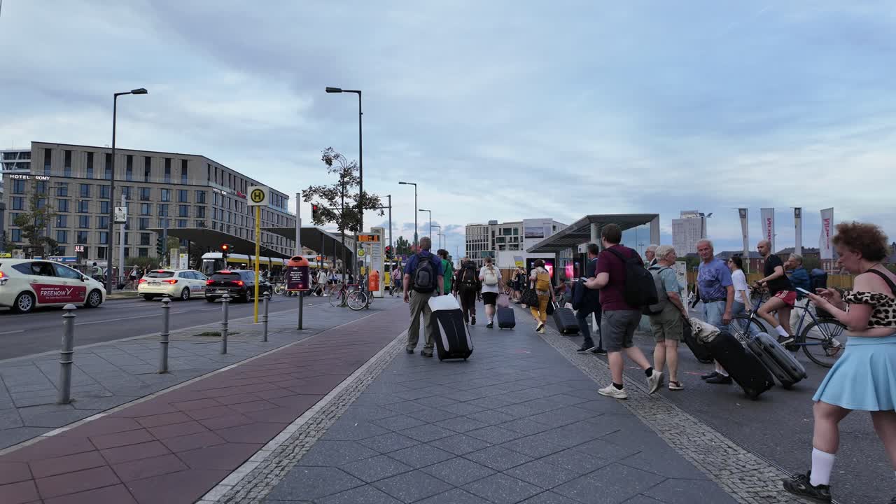 A bustling scene in Berlin's city streets as people pull luggage and cross intersections near transit hubs