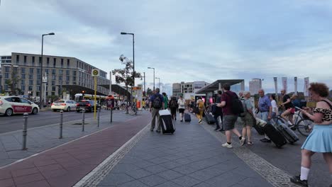 a bustling scene in berlin's city streets as people pull luggage and cross intersections near transit hubs