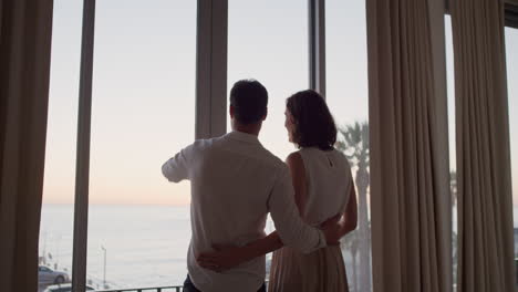 glückliches reisepar kommt im hotelzimmer im urlaub an und schaut aus dem fenster. ein junger mann fotografiert die aussicht und genießt einen romantischen urlaub mit seiner frau.