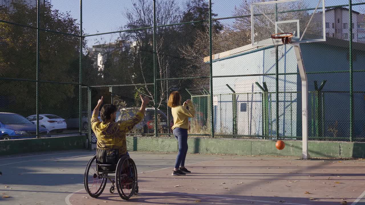 hombre discapacitado feliz jugando al baloncesto con su novia al aire libre en la cancha de baloncesto.