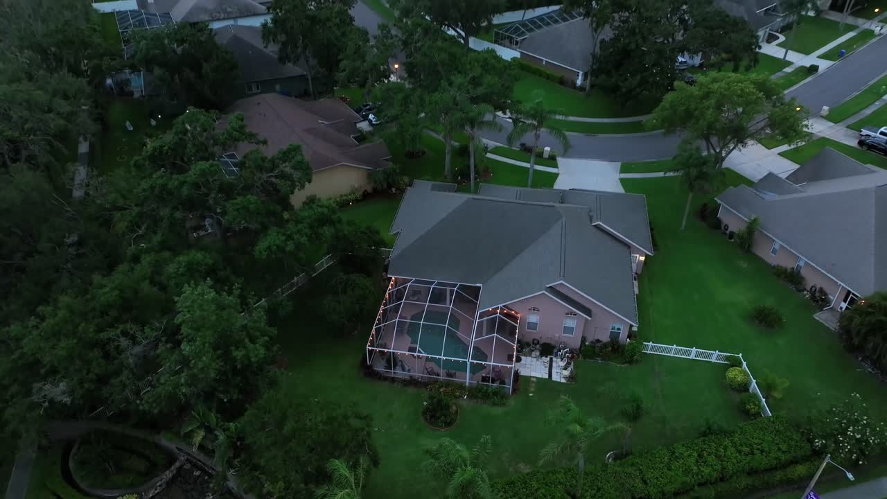 Aerial view of suburban Florida neighborhood at dusk. Single-family homes with screened backyard pools and lush gardens create peaceful tropical residential scene. Luxury homes in suburbia