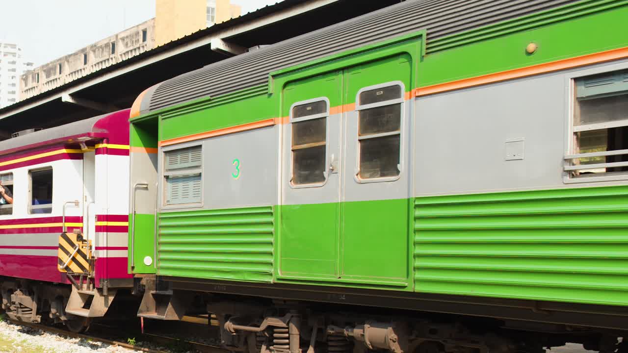 Un treno passeggeri verde e viola parte lentamente da un binario coperto in una stazione ferroviaria