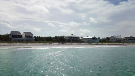 drone flying low towards beach while curving right to reveal a couple sitting on a private beach.