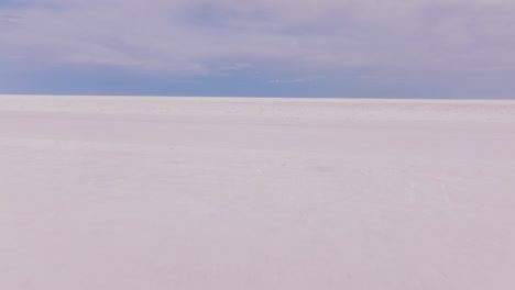 aerial pullback over pristine bonneville salt flats utah with blue sky on horizon above white ground
