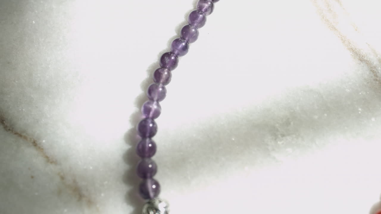 toma deslizante de cuentas de amatista colocadas en una losa de mármol blanco tomada con una plataforma rodante en 4k uhd