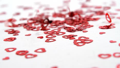 red heart shaped confettis falling down on white surface 4k