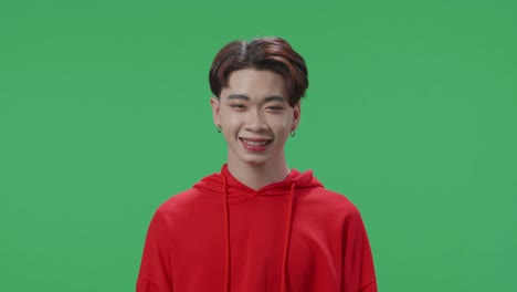 the portrait of a smiling asian transgender male positively shaking her head at the camera in the green screen studio