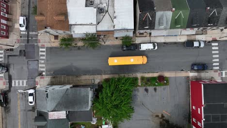 slowly driving yellow bus on street of american town. aerial top down shot. historic homes along american neighborhood. traffic scene after school.