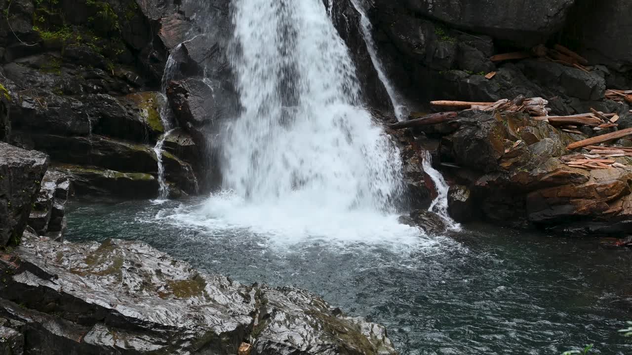 Aerial drone shot of a powerful waterfall cascading over rugged rocks into a clear mountain pool