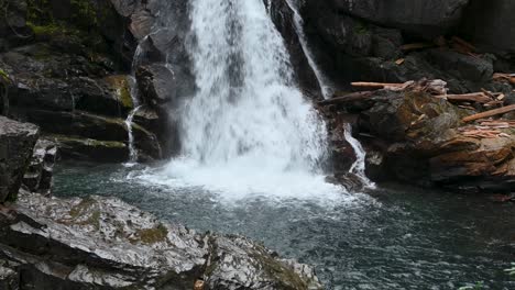 aerial drone shot of a powerful waterfall cascading over rugged rocks into a clear mountain pool