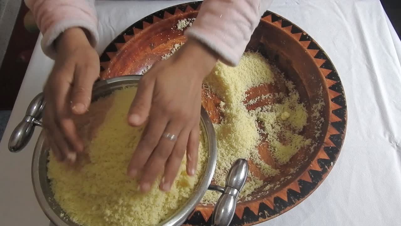 Una mujer coloca la sémola de cuscús en una vaporera para cocinarla al vapor, en casa