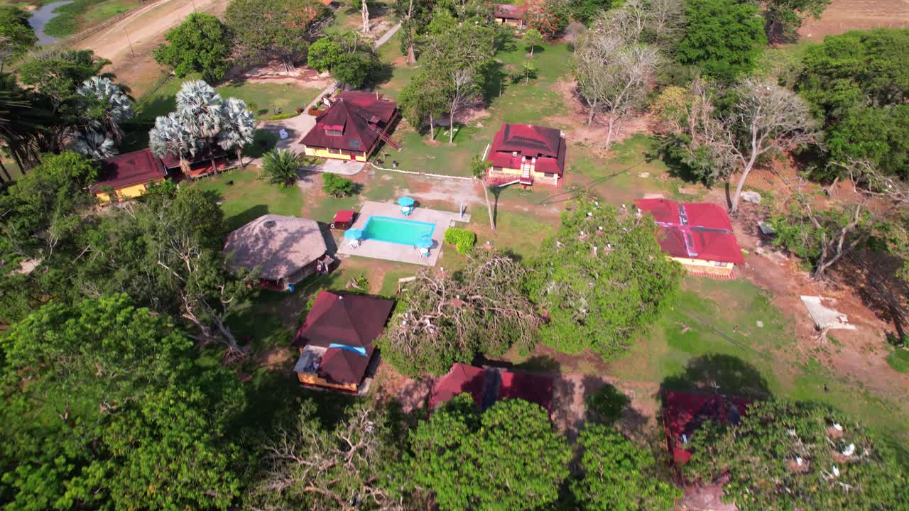 Aerial view of rural farm in Venezuelan Los llanos, featuring several buildings with red roofs and mix of lush green trees and barren, dirt-covered ground