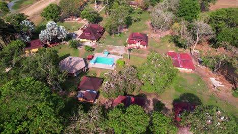 aerial view of rural farm in venezuelan los llanos, featuring several buildings with red roofs and mix of lush green trees and barren, dirt-covered ground