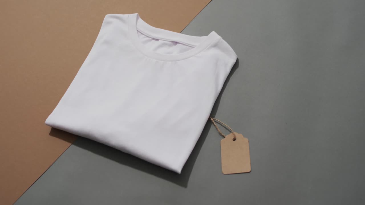 video di strato piatto di maglietta bianca piegata con tag e spazio di copia su sfondo grigio e marrone