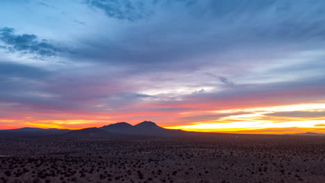 hiperlapso aéreo deslizante sobre o deserto de mojave com montanhas escarpadas à distância durante um nascer do sol colorido