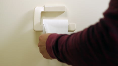 man pulls some toilet paper from the roll hanging on the wall