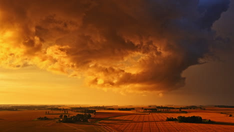 picturesque view of sunset over a vast rural landscape with heavy clouds in sky. orange hue in sky