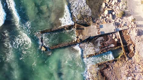 coastal erosion at trenc beach in mallorca spain with damaged building foundation pounded by waves, aerial top view rotation shot