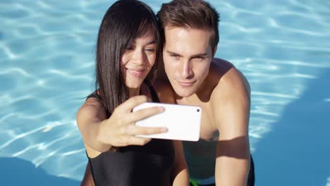 una pareja guapa toma una foto mientras está de pie en la piscina
