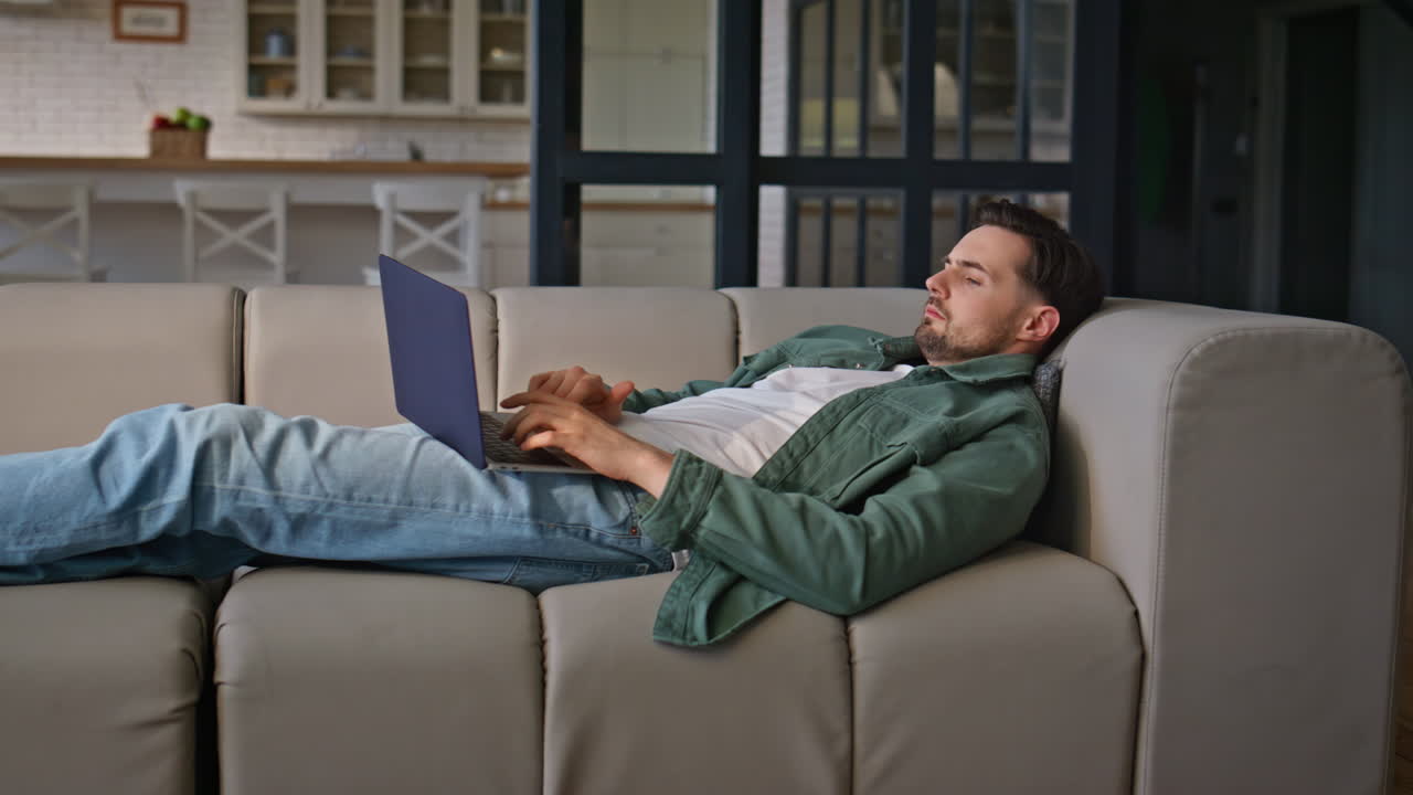 Man working laptop lying comfortable at home couch. Busy guy freelancer work