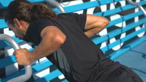 man with dark hair ponytail does incline close grip push ups on outdoor fitness course push up bars, close up