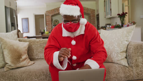 Senior-african-american-man-at-christmas-time-wearing-red-face-mask-and-santa-costume