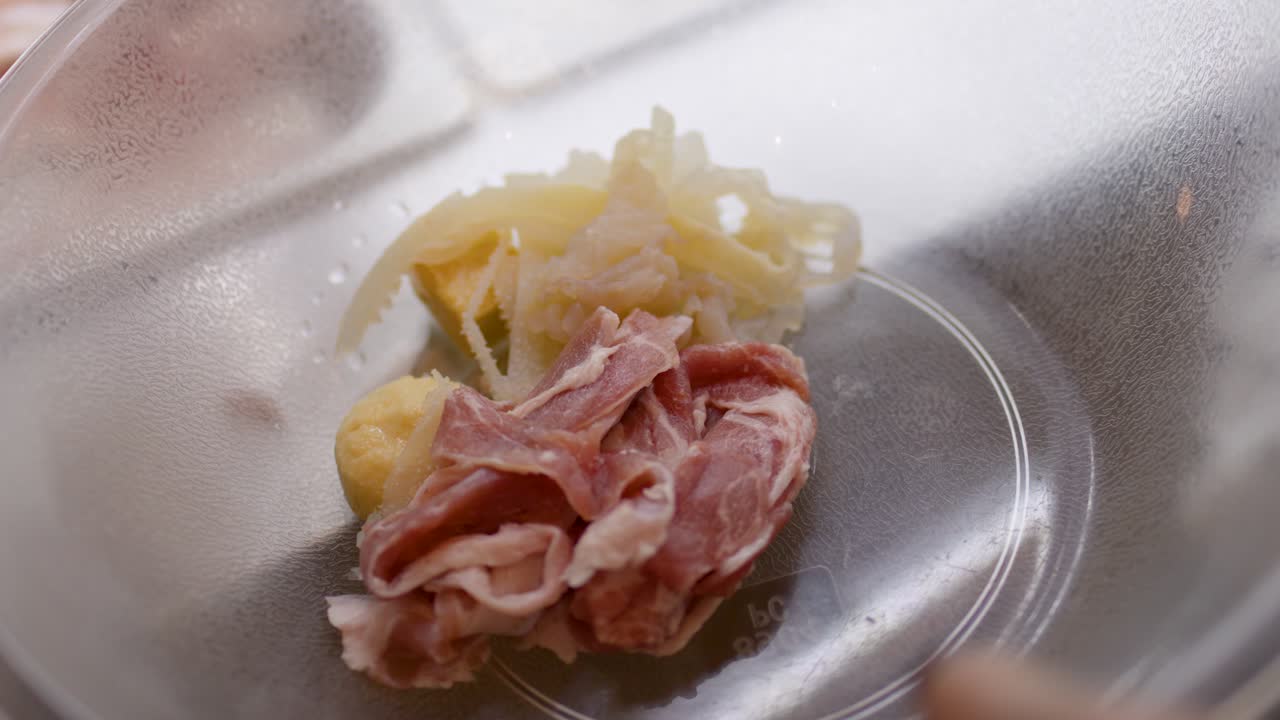 Hand uses tongs to pick raw meat and vegetables from buffet tray under indoor lighting