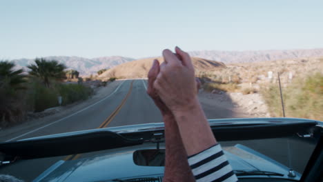 senior couple hold hands in the air, driving in open top car