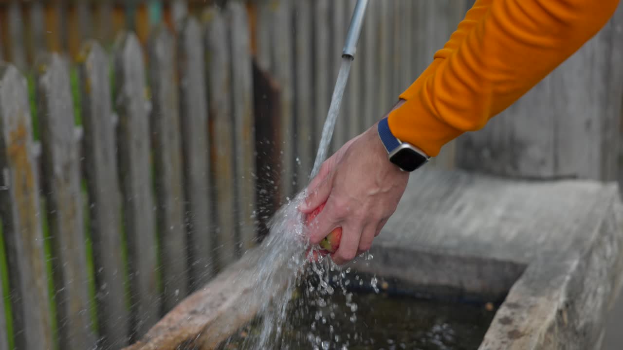 cerca de las manos con chaqueta naranja y reloj inteligente lavando melocotón en la fuente