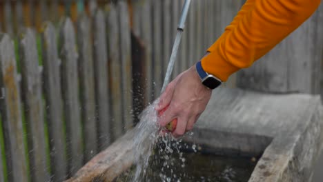 close up of hands wearing orange jacket and smartwatch washing peach on fountain