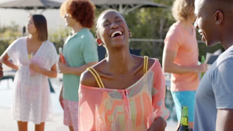 happy african american couple talking in the sun at pool party with diverse friends, slow motion