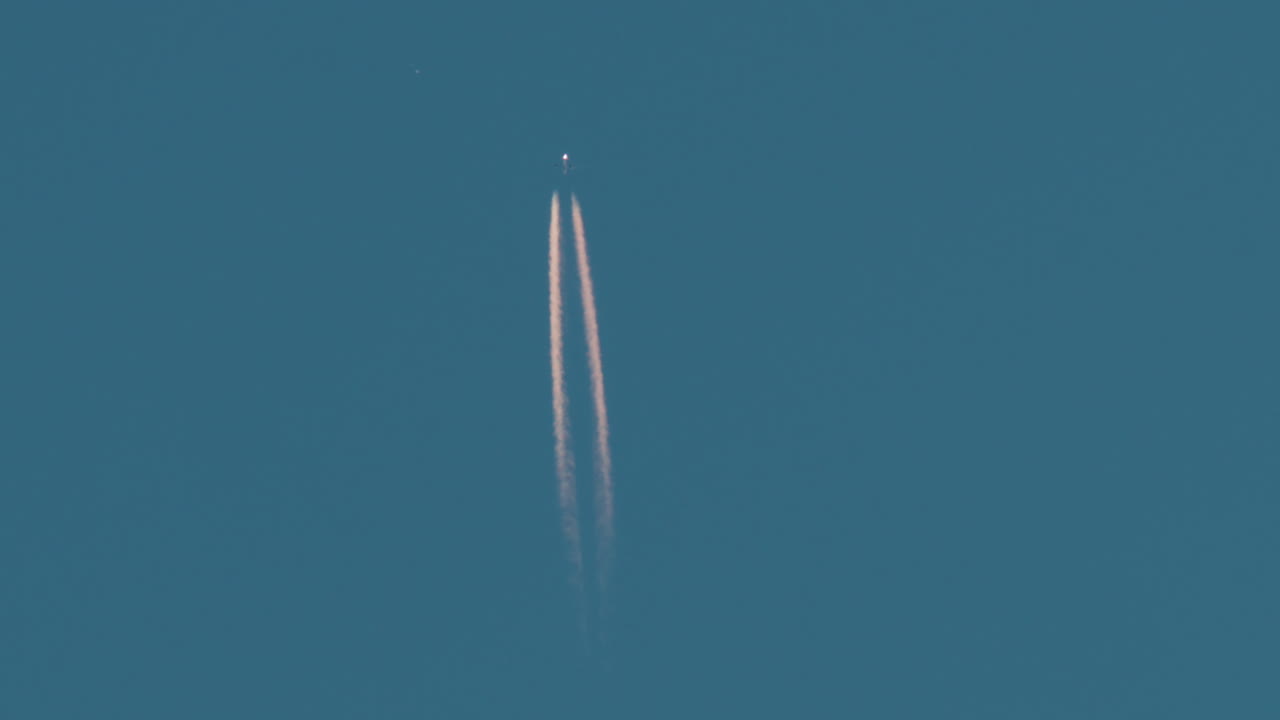 Airplane flying high above leaving long contrails in a clear blue sky
