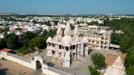 enorme templo indio en una ciudad, con casas a su alrededor, templo swaminarayan, gandhinagar, gran tiro de drones con cielo azul