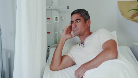 Front-view-of-Caucasian-male-patient-looking-away-while-lying-on-hospital-bed-in-hospital-ward-4k