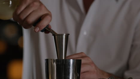 Closeup-shot-of-a-bartender-measuring-liquor-into-a-jigger-and-pouring-it-into-a-metal-shaker