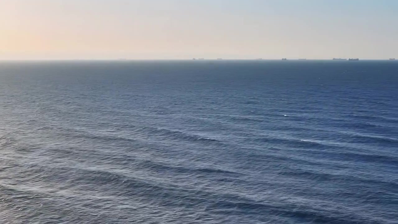 Orizzonte oceanico calmo al bagliore del tramonto, ampia vista aerea di onde e increspature delicate, navi da carico distanti.