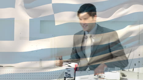 agitando la bandera de grecia contra el joven empresario caucásico celebrando en la oficina