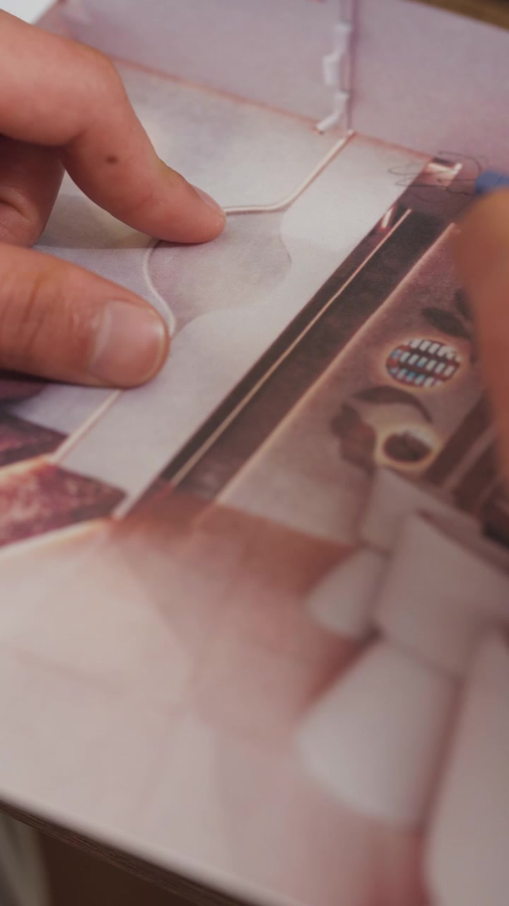 Primo piano che mostra una mano che tiene un foglio con un'immagine di interni, mentre con una matita traccia linee e forme sull'area vuota, abbozzando una proposta.