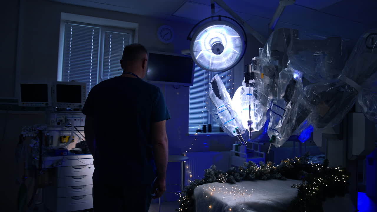 Medical specialist enters the dark surgical room. Da Vinci robotic is in the middle of the room. Christmas decorations and lights on operational table and equipment.
