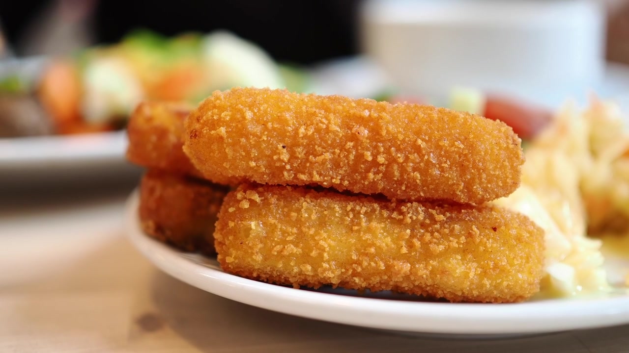 Primo piano di bastoncini di cibo fritto dorati e croccanti su un piatto.
