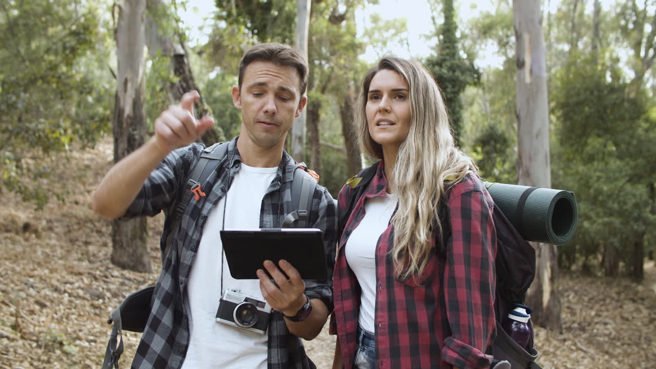 un par de jóvenes mochileros usando una tableta en el bosque