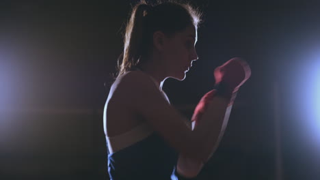 training a beautiful female boxer doing punches in a dark room. steadicam shot. preparation for self-defense and fight in the ring