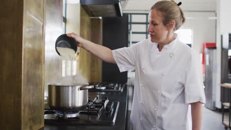 caucasian female chef pouring salt into boiling water