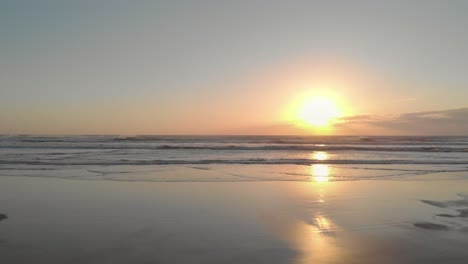 Flying-low-and-slowly-from-a-soft-sandy-beach-towards-an-ocean-at-sunset