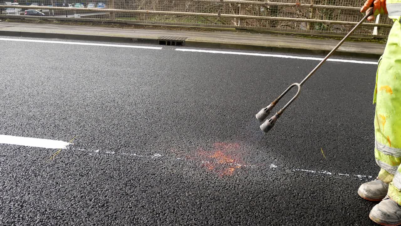 contratista con soplete de llama de gas propano derritiendo pintura de marcado de asfalto de carretera asfaltada