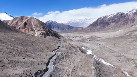 aerial drone shot tracking a car as it crosses a dry riverbed, kicking up dust in ladakh’s desert terrain.