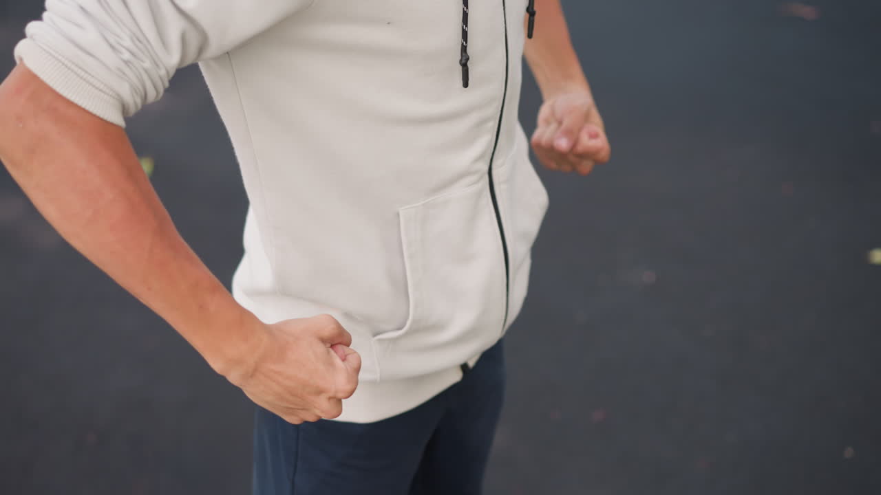 후드티를 입고 있는 젊은 백인 남성, 젖은 아스팔트 위에서 소매를 걷는 손 클로즈업, 흐린 하늘, 흩날리는 낙엽, 분위기 있는 영화 같은 톤, 캐주얼한 스트리트 패션, 사색에 잠긴 자세, 옷감 질감